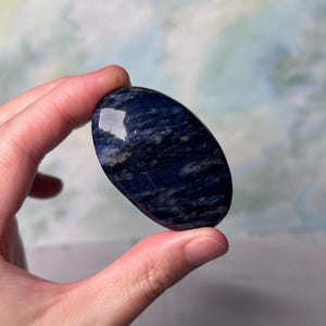 Puede incluir: Una piedra de lapisl&aacute;zuli azul lisa de forma ovalada con vetas blancas y grises. La piedra est&aacute; pulida y tiene un acabado brillante.