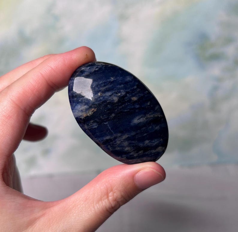Puede incluir: Una piedra de lapisl&aacute;zuli azul lisa de forma ovalada con vetas blancas y grises. La piedra est&aacute; pulida y tiene un acabado brillante.