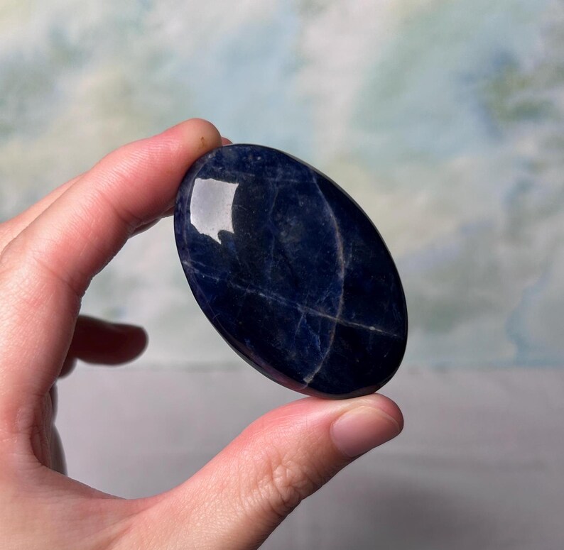 Puede incluir: Una piedra preciosa azul lisa de forma ovalada con vetas blancas. La piedra preciosa est&aacute; pulida y tiene un acabado brillante.