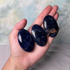 Puede incluir: Tres piedras de sodalita azul lisas de forma ovalada con vetas blancas. Las piedras est&aacute;n pulidas y tienen un acabado brillante.