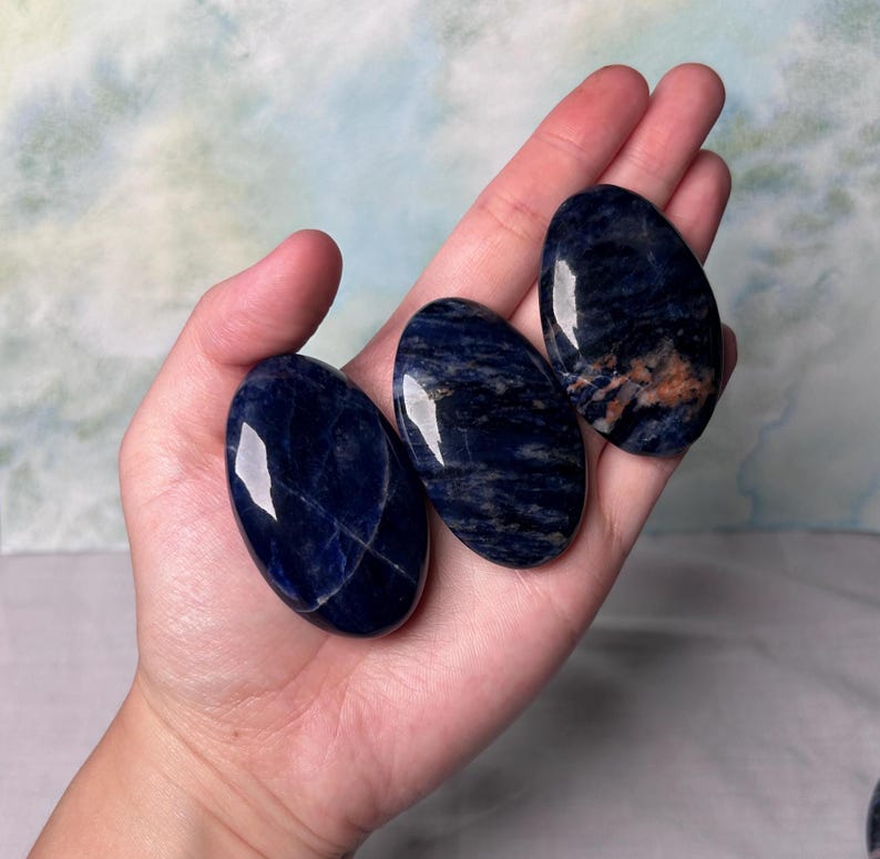 Puede incluir: Tres piedras de sodalita azul lisas de forma ovalada con vetas blancas. Las piedras est&aacute;n pulidas y tienen un acabado brillante.