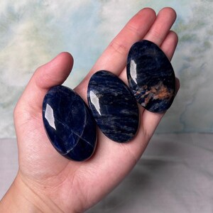 Puede incluir: Tres piedras de sodalita azul lisas de forma ovalada con vetas blancas y marrones. Las piedras est&aacute;n pulidas y tienen un acabado brillante.