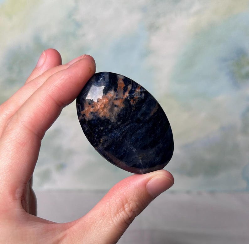 May include: A smooth, oval-shaped blue and orange gemstone with a swirling pattern. The stone is polished and has a glossy finish.