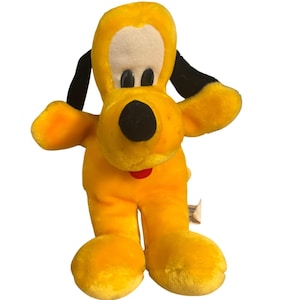 May include: A plush toy of Pluto, a yellow dog with black ears and a black nose. The toy has a white face and a red tongue. The toy is standing with its arms outstretched.
