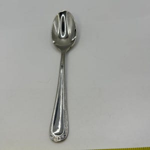 May include: A silver spoon with a rounded bowl and a long, slender handle. The handle is decorated with a beaded pattern along the edges. The spoon is made of a shiny, reflective metal.