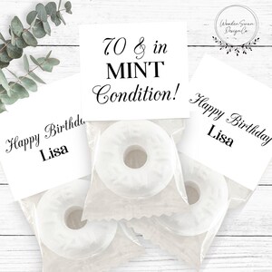 Op de afbeelding: Drie witte mintsnoepjes in doorzichtige plastic verpakkingen, elk bevestigd aan een witte kaart. Eén kaart leest 70 & in MINT Condition! en twee kaarten lezen Happy Birthday Lisa. Een rond logo staat in de rechterbovenhoek.