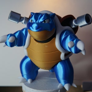 以下が含まれることがあります： 銃を背負った亀のようなポケモンのキャラクターの青と茶色の3Dプリントフィギュア