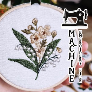 Puede incluir: Un aro de bordado blanco con un diseño floral que presenta flores blancas y beige y hojas verdes. El aro está etiquetado como "MACHINE EMBROIDERY FILE".