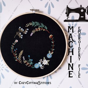 May include: A black embroidery hoop with a floral design stitched in shades of blue, green, and white. The hoop is on a white background with a blue and white pattern. The text "MACHINE EMBROIDERY FILE" is written vertically in black on the right side of the image. The text "BY COZYCOTTAGE STITCHES" is written in black at the bottom of the image.