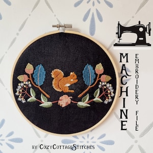 Puede incluir: Un aro de bordado negro con un diseño bordado colorido de una ardilla en un árbol con hojas y bayas. El texto "MACHINE EMBROIDERY FILE" está escrito verticalmente en el lado derecho del aro. El texto "BY COZYCOTTAGE STITCHES" está escrito debajo del aro.