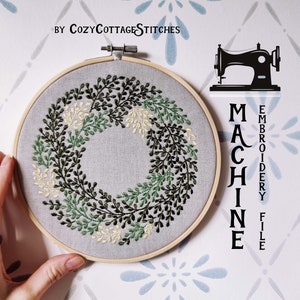 Può includere: Un cerchio da ricamo con un disegno floreale verde e bianco, con il testo "MACHINE EMBROIDERY FILE" sul lato destro dell'immagine.