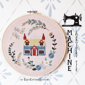 May include: A pink embroidery hoop with a machine embroidery design of a blue cottage with a red door and yellow roof surrounded by flowers and greenery. The text "MACHINE EMBROIDERY FILE" is on the right side of the hoop. The text "BY COZYCOTTAGE STITCHES" is below the hoop.