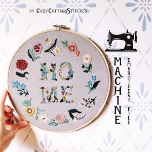 May include: A gray embroidery hoop with the words "HOME" and "ME" stitched in colorful floral designs. The hoop is surrounded by various embroidered flowers. The text "MACHINE EMBROIDERY FILE" and a sewing machine graphic are on the right.