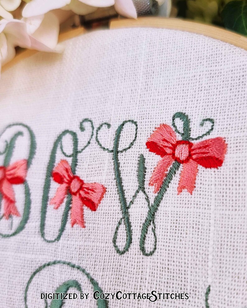 May include: Embroidered design of the word "Baby" with green lettering and pink bows. The design is on a white fabric background.