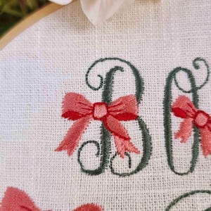 May include: Embroidered hoop art with the word "Baby" in cursive script with pink bows around each letter. The text "Digitized by CozyCottageStitches" is at the bottom of the hoop.