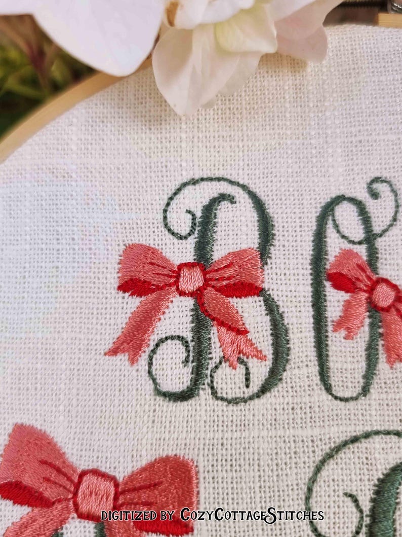 May include: Embroidered hoop art with the word "Baby" in cursive script with pink bows around each letter. The text "Digitized by CozyCottageStitches" is at the bottom of the hoop.