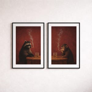 Op de afbeelding: Twee ingelijste kunstdrukken. Eén toont een wasbeer, de andere een aap, beide roken sigaretten en zitten aan een tafel met een glas whisky. De achtergrond is dieprood.