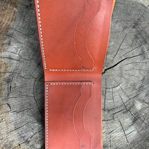 Peut inclure: Un portefeuille en cuir marron avec plusieurs emplacements pour cartes et un porte-billets. Le portefeuille est ouvert et l'intérieur est visible.