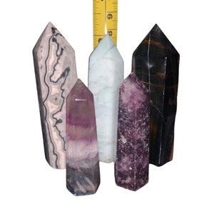 May include: Five different crystal points, including a black and white banded point, a light blue point, a purple point, a dark purple point, and a black point. The points are arranged in a row and are all about the same size.