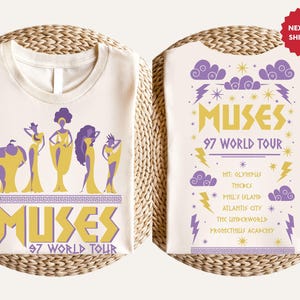 Peut inclure: Un t-shirt blanc avec un motif violet et or représentant le texte "MUSES 97 WORLD TOUR". Le devant du t-shirt montre un groupe de femmes en silhouettes violettes et or. Le dos du t-shirt montre une liste de dates de tournée en texte violet et or.