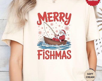May include: Cream-colored t-shirt with a graphic of Santa Claus fishing from a boat. The text "MERRY FISHMAS" is in red above and below the illustration. Red snowflakes are scattered around the text.