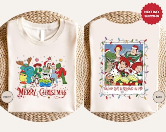 May include: Off-white t-shirts featuring Toy Story characters in Christmas attire. The front shirt reads "MERRY CHRISTMAS" in red script. The back shirt has the text "You've got a friend in me" with a festive border.