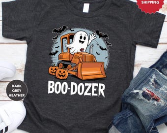 Peut inclure: T-shirt gris foncé chiné avec un motif sur le thème d'Halloween. Le dessin représente un fantôme de dessin animé conduisant un bulldozer orange, avec deux citrouilles et des chauves-souris. Le texte "BOO-DOZER" est imprimé en blanc.