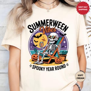 May include: Cream-colored t-shirt with a graphic featuring a skeleton in sunglasses relaxing in a beach chair, holding a drink. The design includes pumpkins, bats, and the text "Summerween Vibes Spooky Year Round."