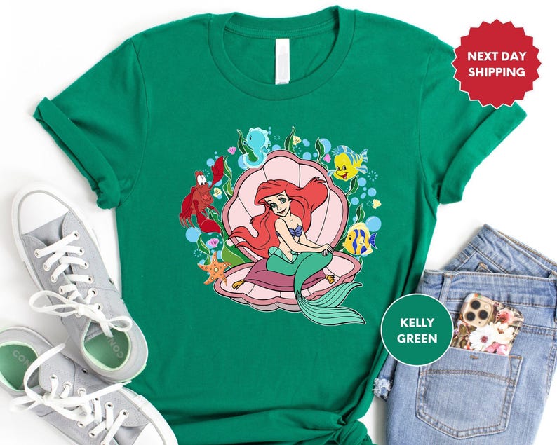 a green shirt with an image of a little mermaid on it