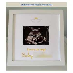 May include: White framed fabric mat with an ultrasound image. The mat features embroidered angel wings and the words "forever our angel" and "Baby" in gold script. The text "Embroidered Fabric Frame Mat" is at the top.