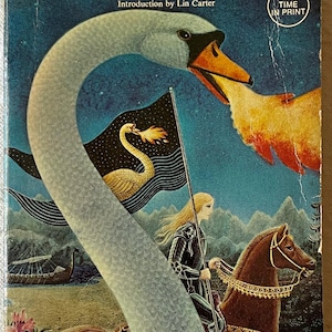 Op de afbeelding: Vintage paperback boekomslag voor "Merlin's Ring" van H. Warner Munn. De coverkunst toont een zwaan, een ridder te paard en een vlag met een zwaanontwerp. Het boek is gelabeld "First Time in Print".