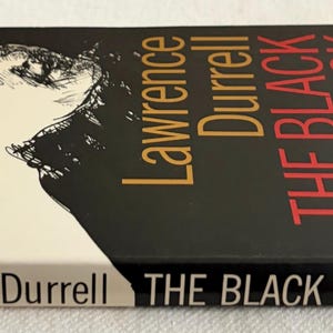 Puede incluir: Un libro de bolsillo titulado "THE BLACK BOOK" de Lawrence Durrell. La portada presenta una ilustraci&oacute;n en blanco y negro de un rostro y el t&iacute;tulo en letras rojas y doradas. El lomo tambi&eacute;n muestra el t&iacute;tulo.