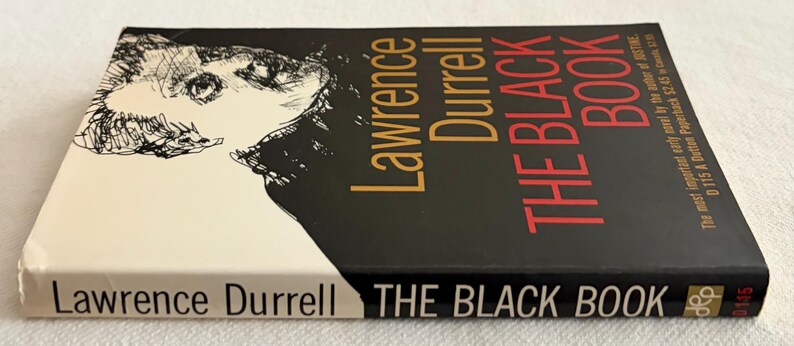 Puede incluir: Un libro de bolsillo titulado "THE BLACK BOOK" de Lawrence Durrell. La portada presenta una ilustraci&oacute;n en blanco y negro de un rostro y el t&iacute;tulo en letras rojas y doradas. El lomo tambi&eacute;n muestra el t&iacute;tulo.