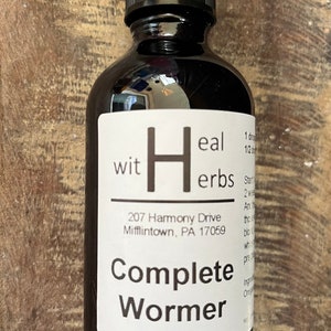 May include: A dark amber glass bottle with a black dropper cap and a white label. The label features the text "wit Heal herbs", "207 Harmony Drive Mifflintown, PA 17059", and "Complete Wormer" in black font, along with additional partial text.