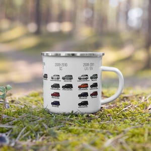 May include: White enamel mug featuring car illustrations and text. The mug displays various car models from 2009-2011, with color names below each car. The mug has a silver rim and a white handle.
