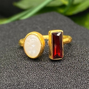 Könnte beinhalten: Goldring mit einem weißen ovalen Stein und einem roten rechteckigen Stein.