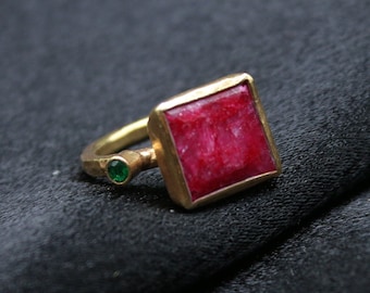Può includere: Un anello d'oro con una pietra rossa quadrata e due pietre verdi più piccole.