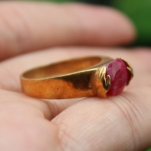 Op de afbeelding: Een gouden ring met een grote, ovale, rode edelsteen in het midden.