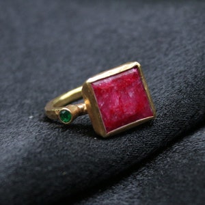 May include: A gold ring with a square red gemstone and two smaller green gemstones.