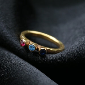 May include: A gold ring with three small gemstones: red, blue, and dark blue.