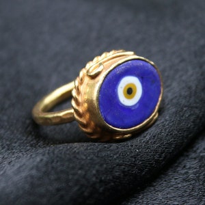 May include: A gold ring with a blue evil eye charm. The charm has a white center with a black pupil.