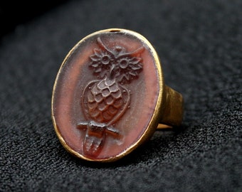 May include: A gold ring with a red carnelian stone featuring a carved owl design.