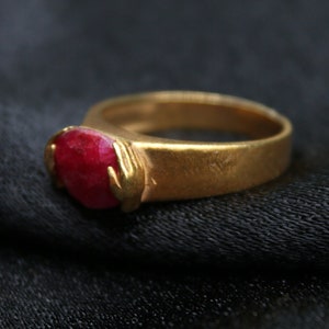 Può includere: Un anello d'oro con una pietra preziosa rossa incastonata al centro. L'anello è su uno sfondo di tessuto nero.