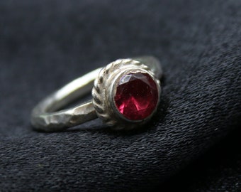 May include: A silver ring with a textured band and a red gemstone.