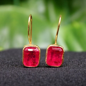 May include: A pair of gold earrings with red gemstone drops. The earrings have a simple design and are perfect for everyday wear.