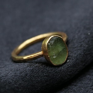 May include: A gold ring featuring a green oval gemstone. The ring has a hammered finish.