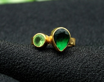 May include: A gold ring with two green gemstones. The larger gemstone is a teardrop shape and the smaller gemstone is round.