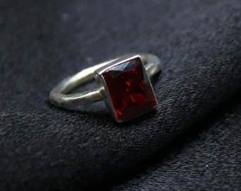 May include: A silver ring with a rectangular red gemstone.