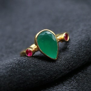 May include: A gold ring with a teardrop-shaped green gemstone and two smaller red gemstones.