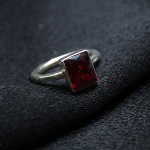 May include: A silver ring with a rectangular red gemstone.